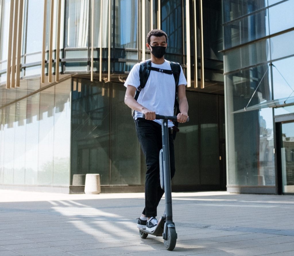 A person wearing a black mask and moving around in an e-scooter